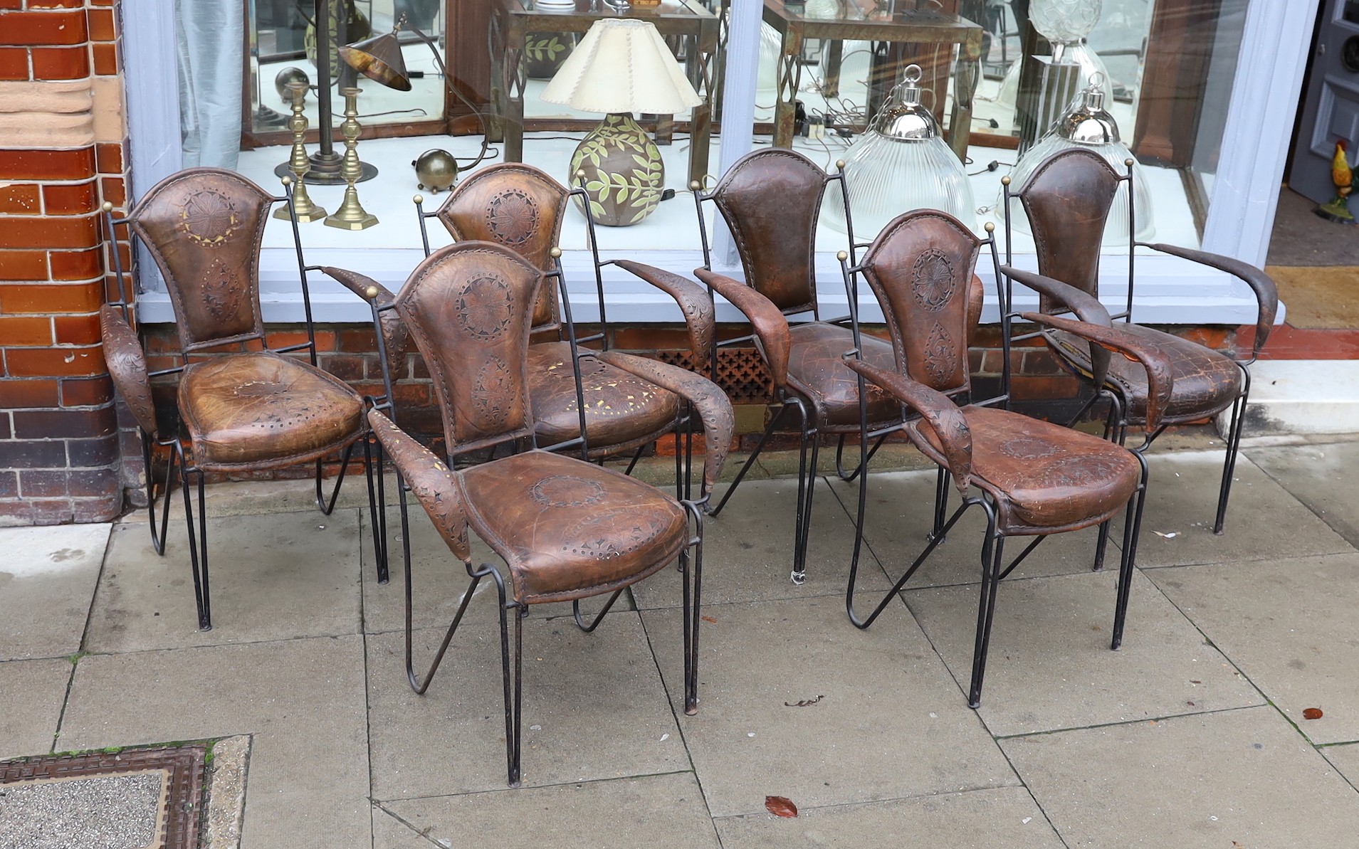 A set of six French wrought iron and brown leather elbow chairs, with brass ball finials, four with tooled and pierced decoration the others plain, height 84cm. width 61cm